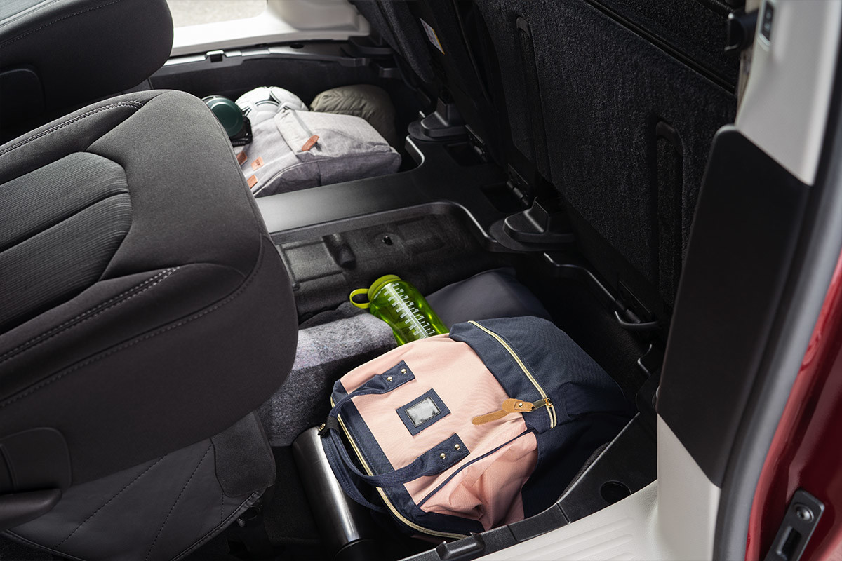 A close-up of a floor storage compartment inside the 2021 Chrysler Grand Caravan packed with athletic equipment, bags and a water bottle.