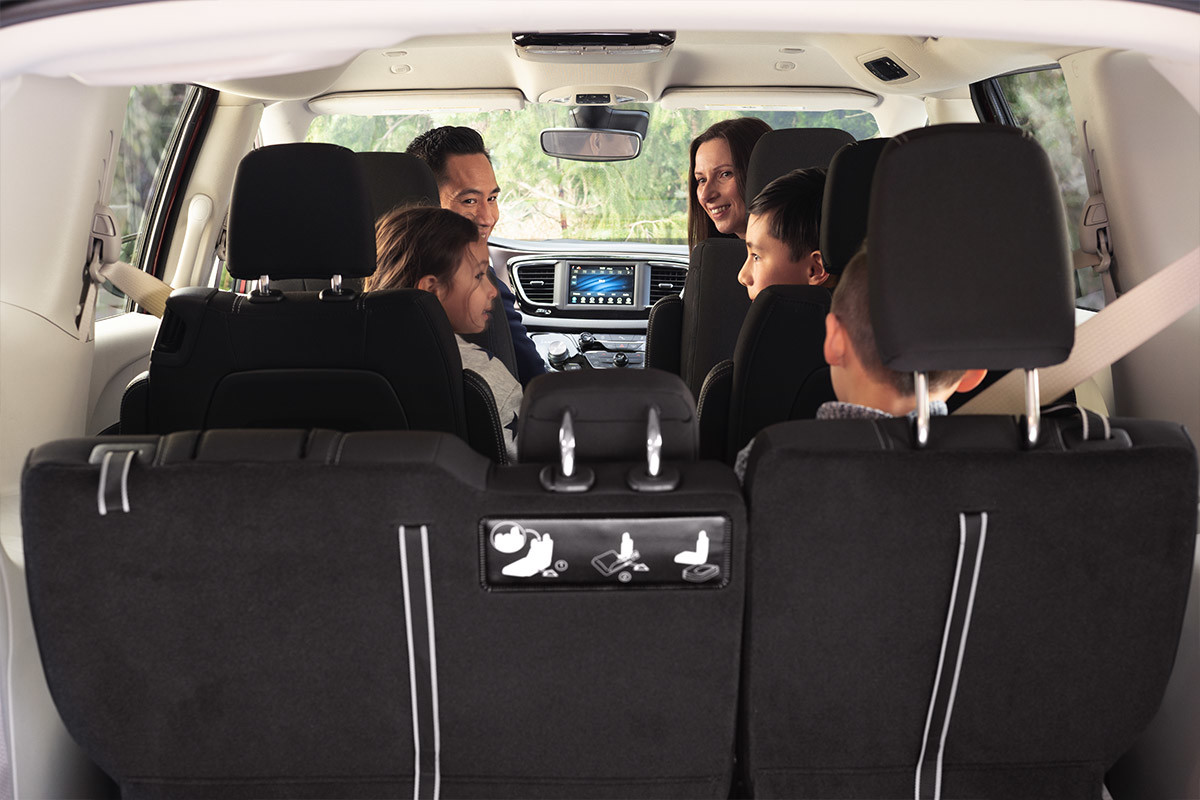 Vue de l’espace utilitaire spacieux à l’intérieur d’une Chrysler Grand Caravan 2021. Un homme et une femme regardent des enfants assis dans les deuxièmes et troisièmes rangées de sièges.