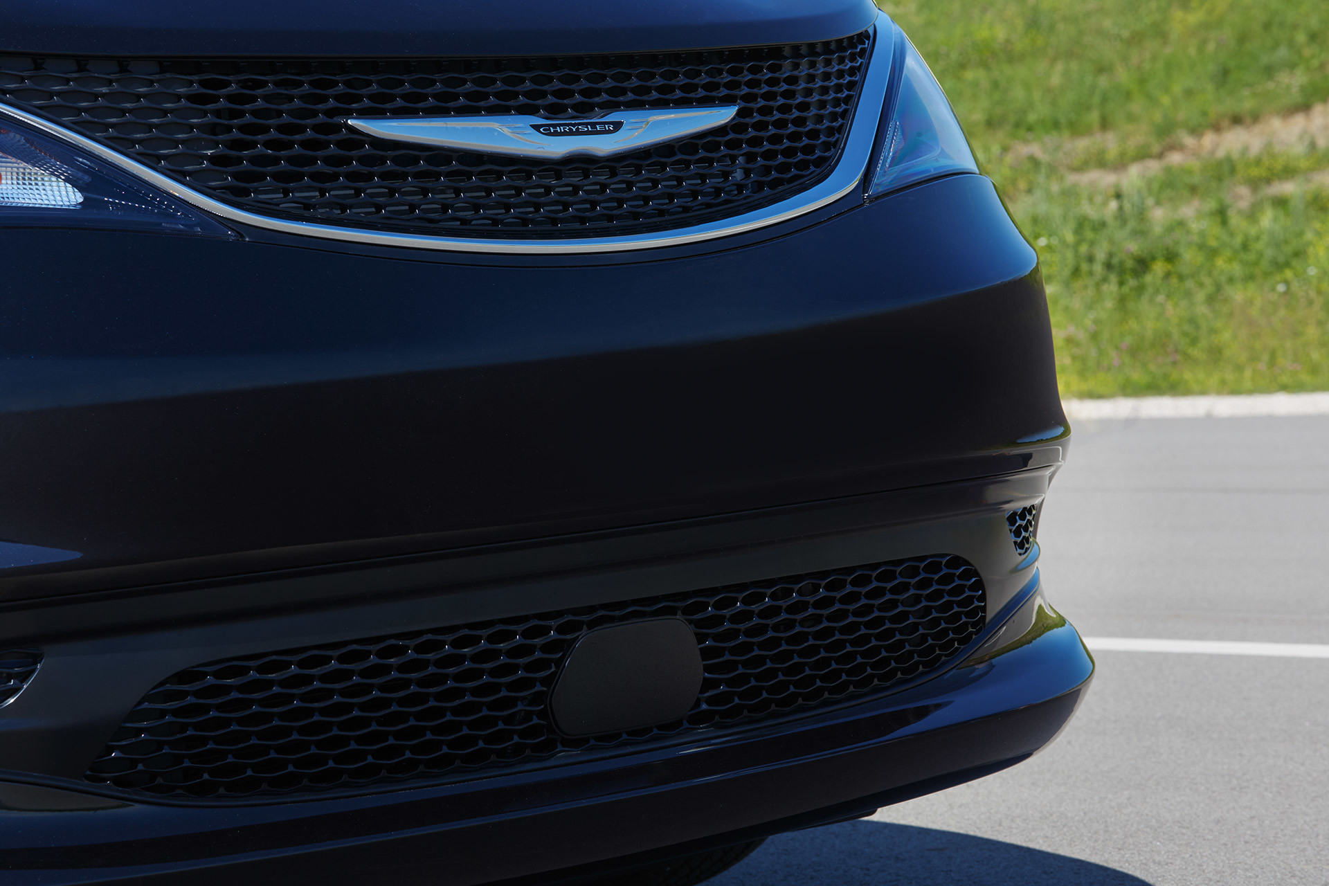 Gros plan du bouclier avant et du légendaire emblème ailé Chrysler d’une Chrysler Grand Caravan 2021 à couche nacrée cristal noir étincelant.