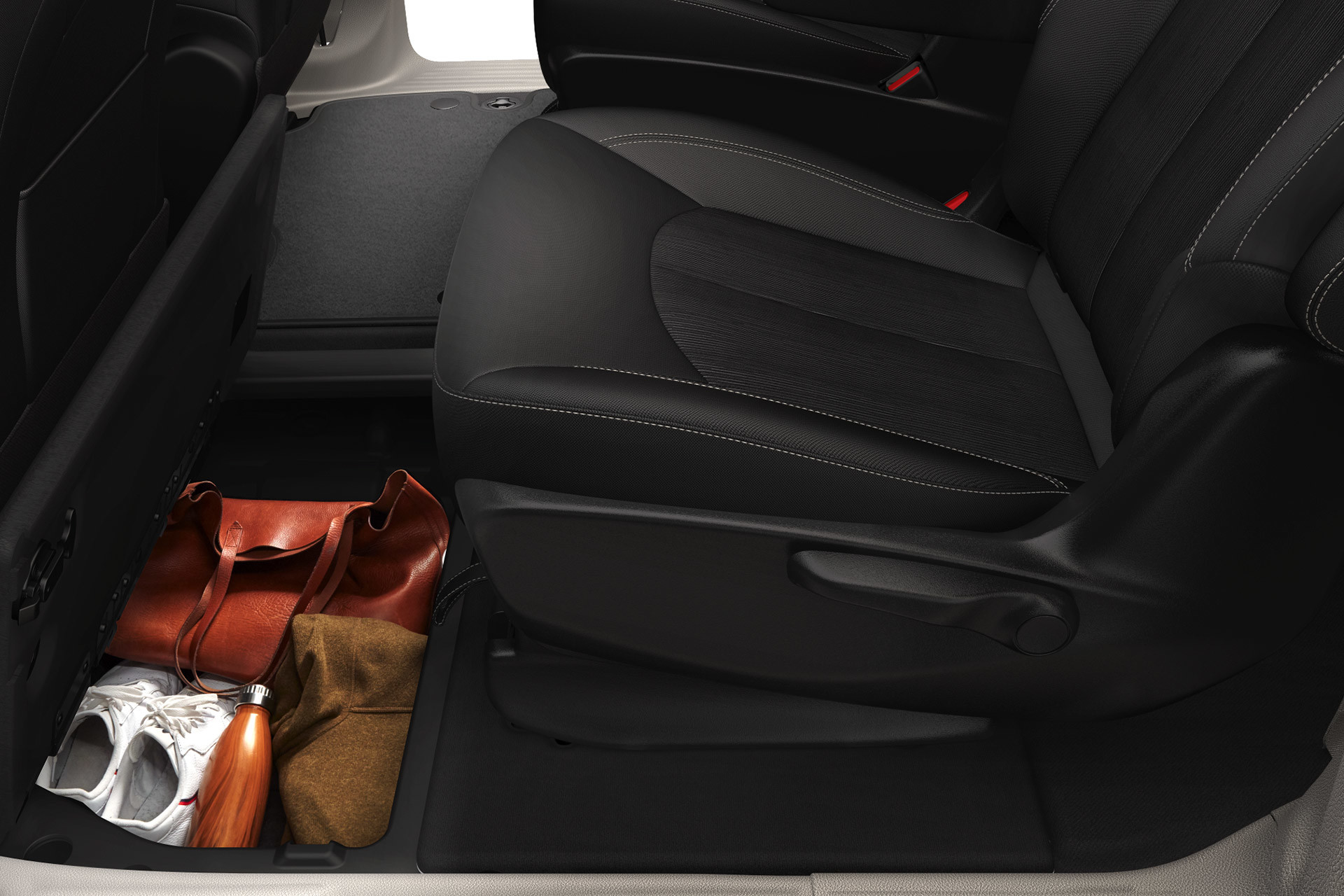 Gros plan d’un compartiment de rangement sous le plancher de la Chrysler Grand Caravan 2021, contenant des chaussures de course, des sacs et une bouteille d’eau.