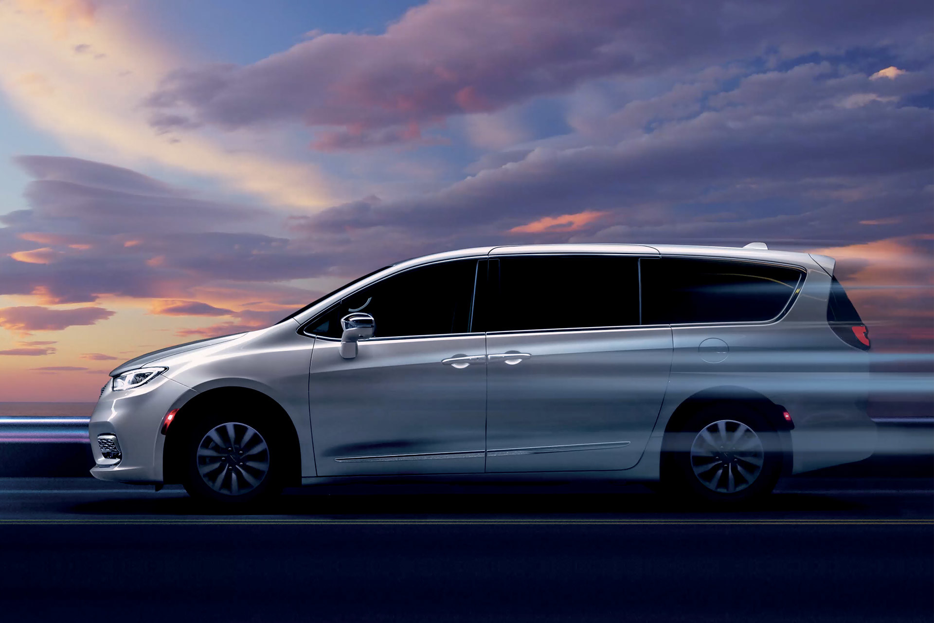 Profile view of a white 2023 Chrysler driving against a purple and pink sunset in the background.