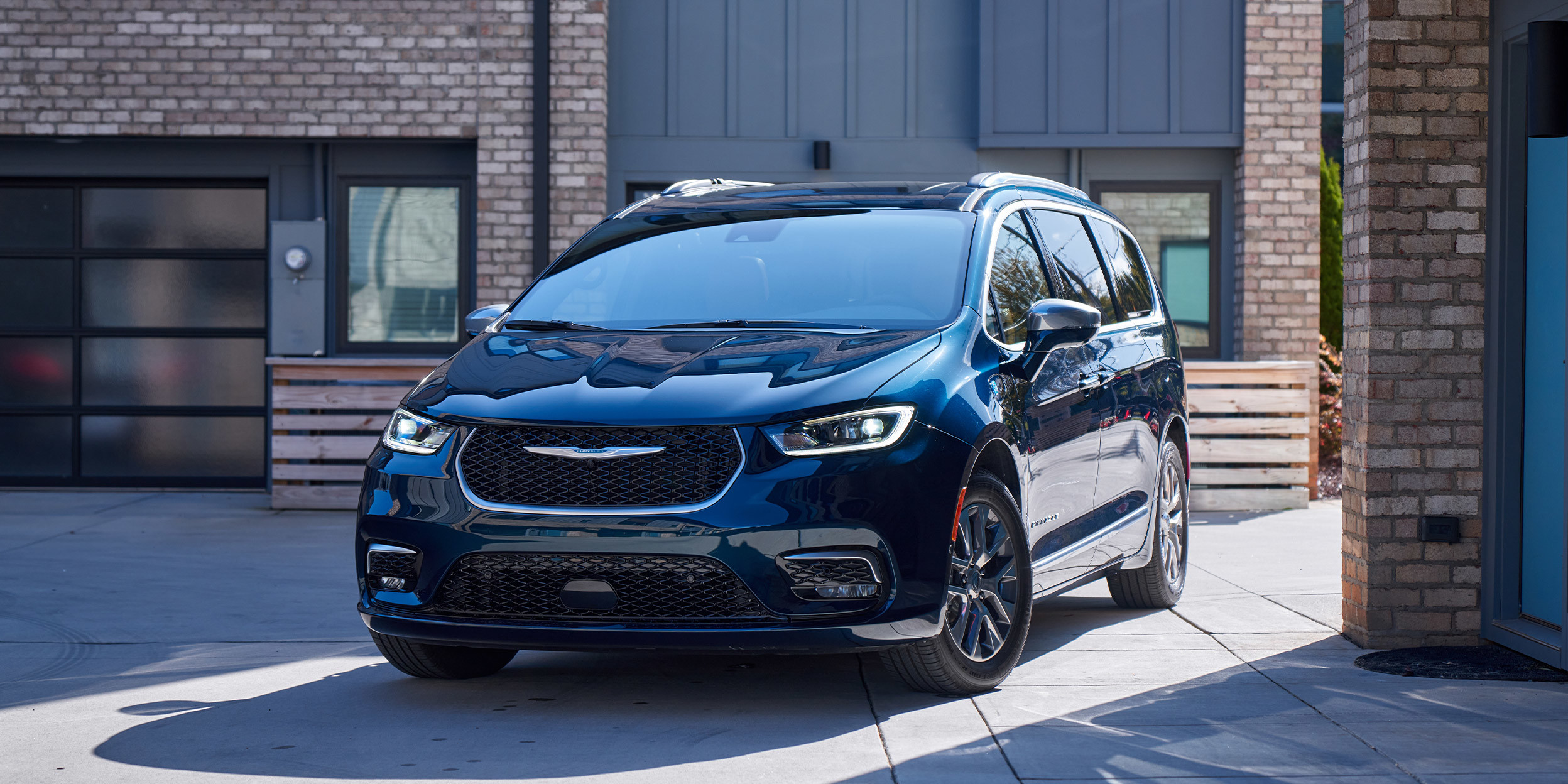 A black Chrysler Pacifia, parked in front of a modern-style house.