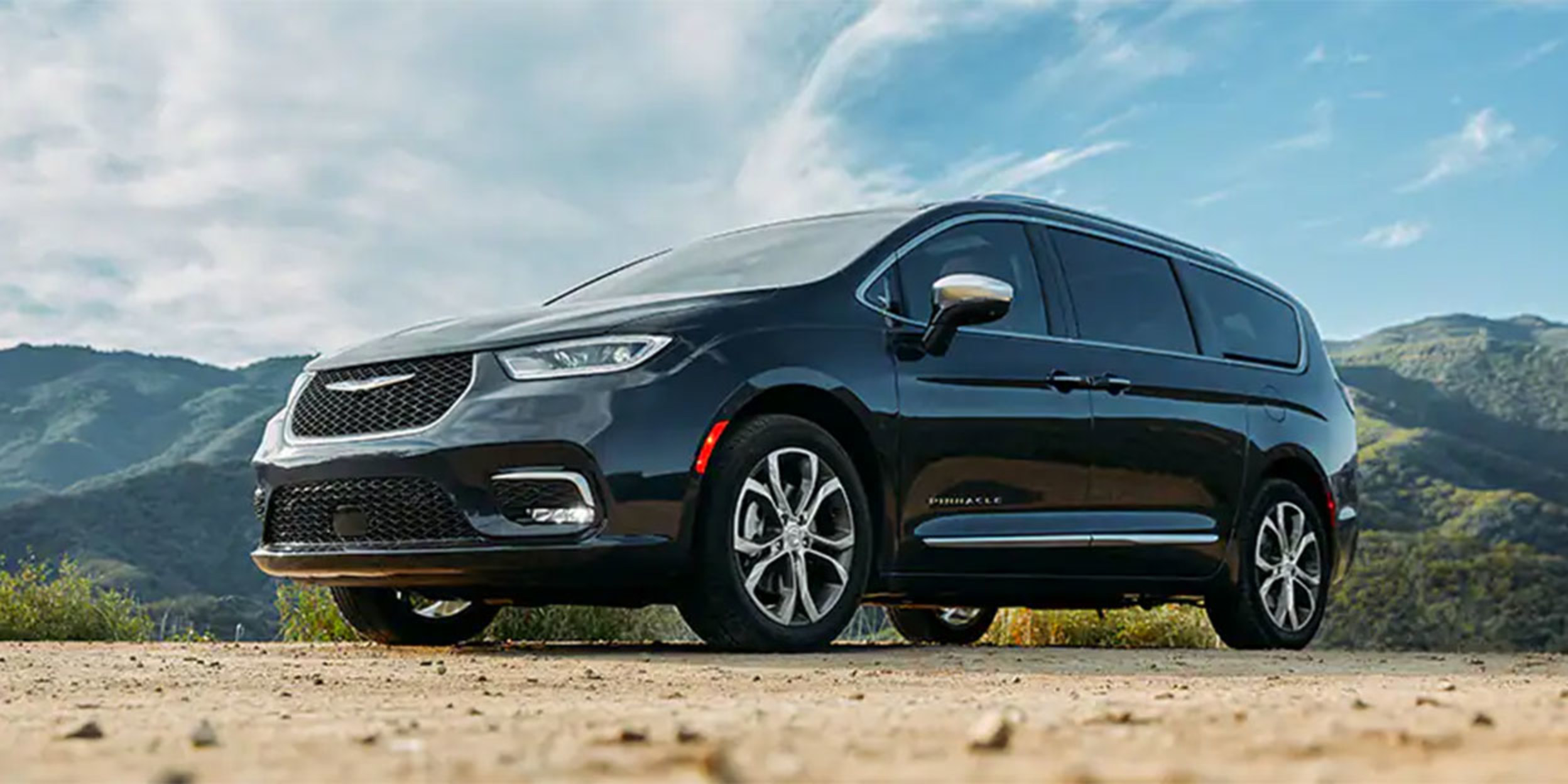 Black Chrysler Pacifica Hybrid parked on rocky road with mountains in the background.