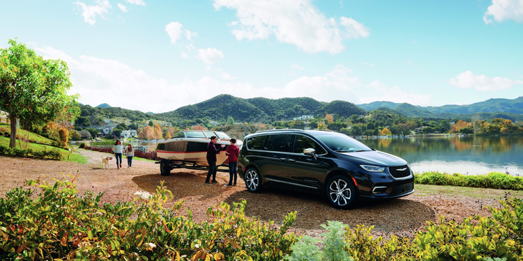 Quatre personnes debout près d’une Chrysler Pacifica Pinnacle noire de 2023, garée sur un chemin de terre, un petit bateau accroché à l’arrière du véhicule, avec vue sur un lac et des montagnes en arrière plan.