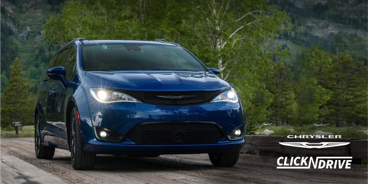 Chrysler Click ’n Drive. Blue Chrysler Pacifica driving on a road with trees and mountains in the background.