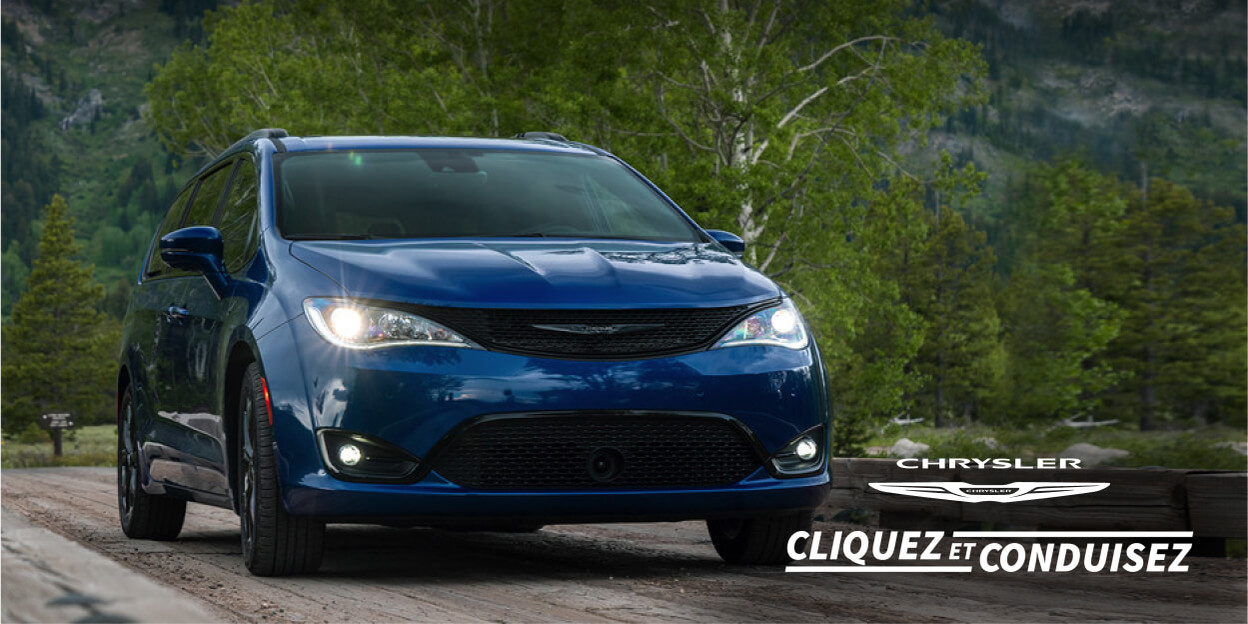 Chrysler Cliquez et Conduisez. Chrysler Pacifica bleue roulant sur une route avec des arbres et des montagnes en arrière-plan.