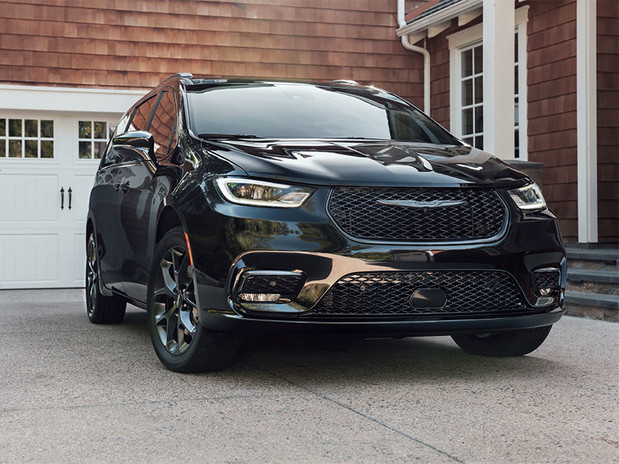 A front view of a black 2023 Chrysler Pacifica parked outside of a residential home with white doors and windows.