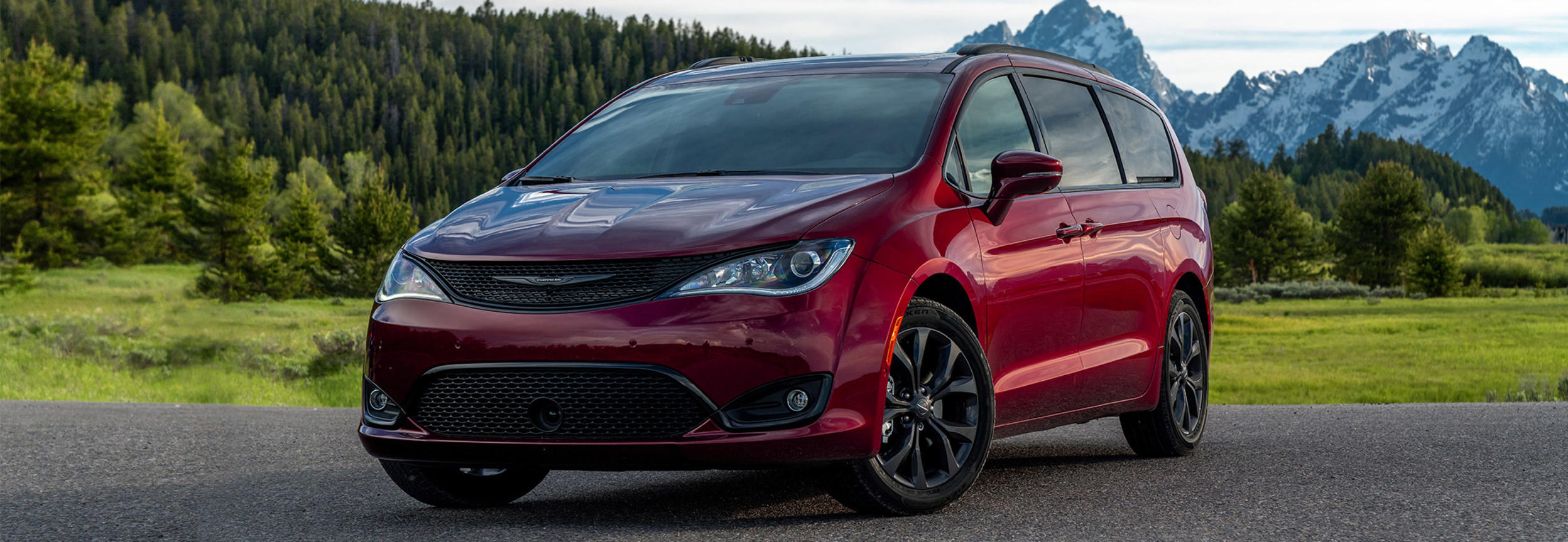 Red 2020 Chrysler Pacifica parked on a paved road surrounded by evergreen and mountains