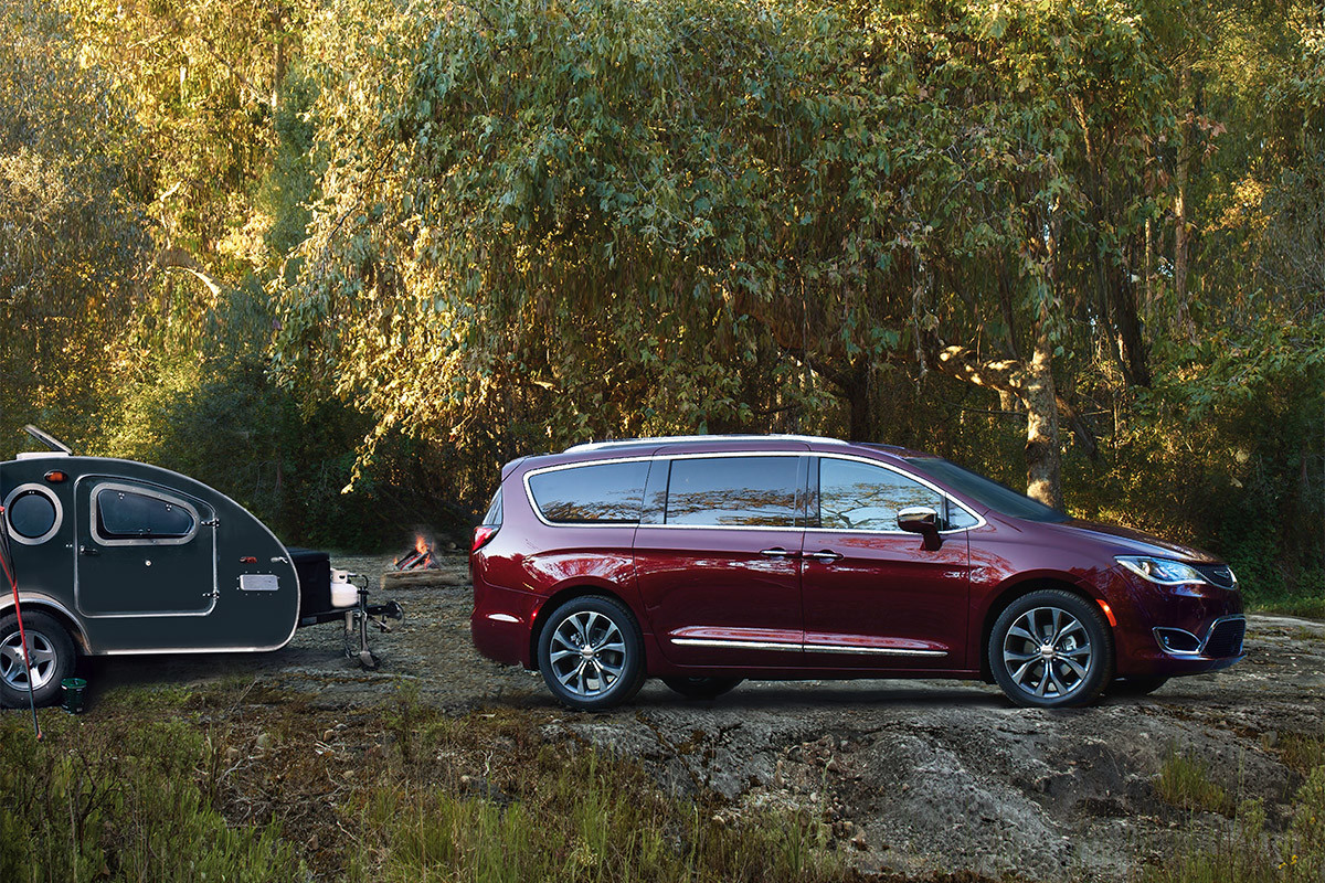 Une Chrysler Pacifica 2020 rouge remorquant un petit véhicule récréatif à travers bois.