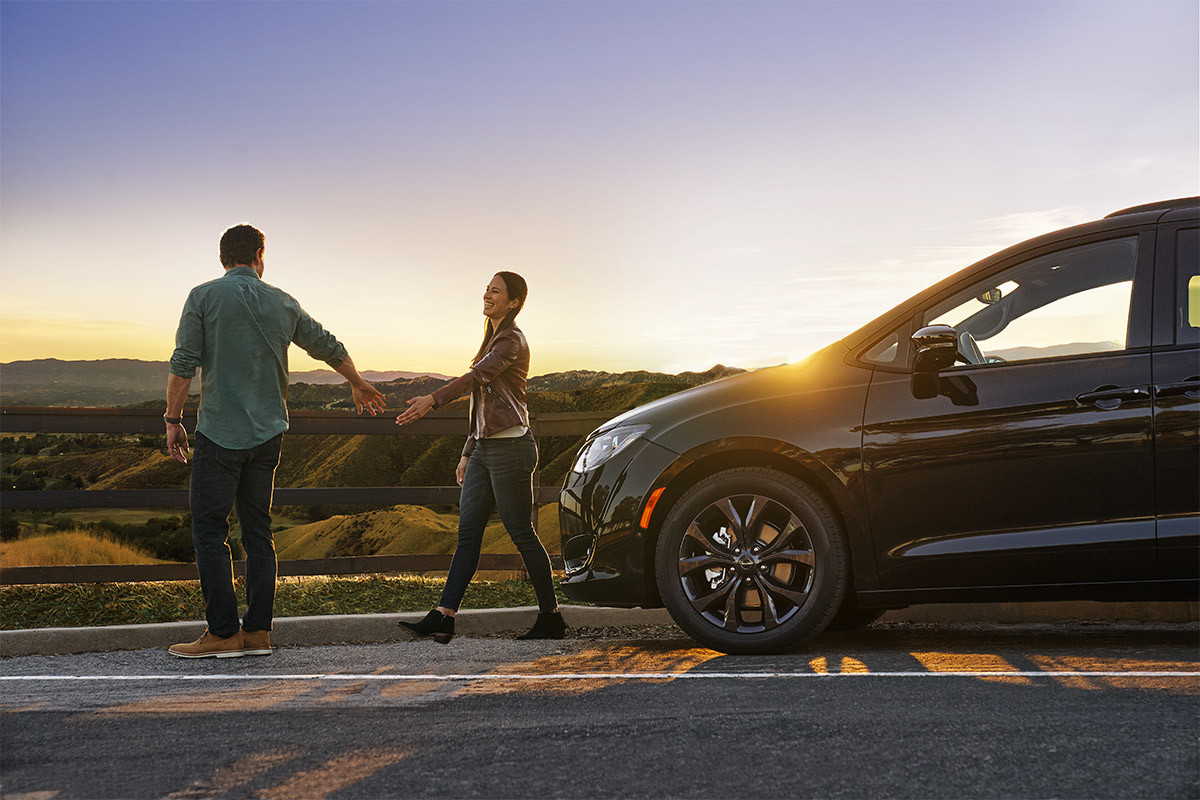 Two people walking on the road with a 2020 Chrysler Pacifica parked behind them.