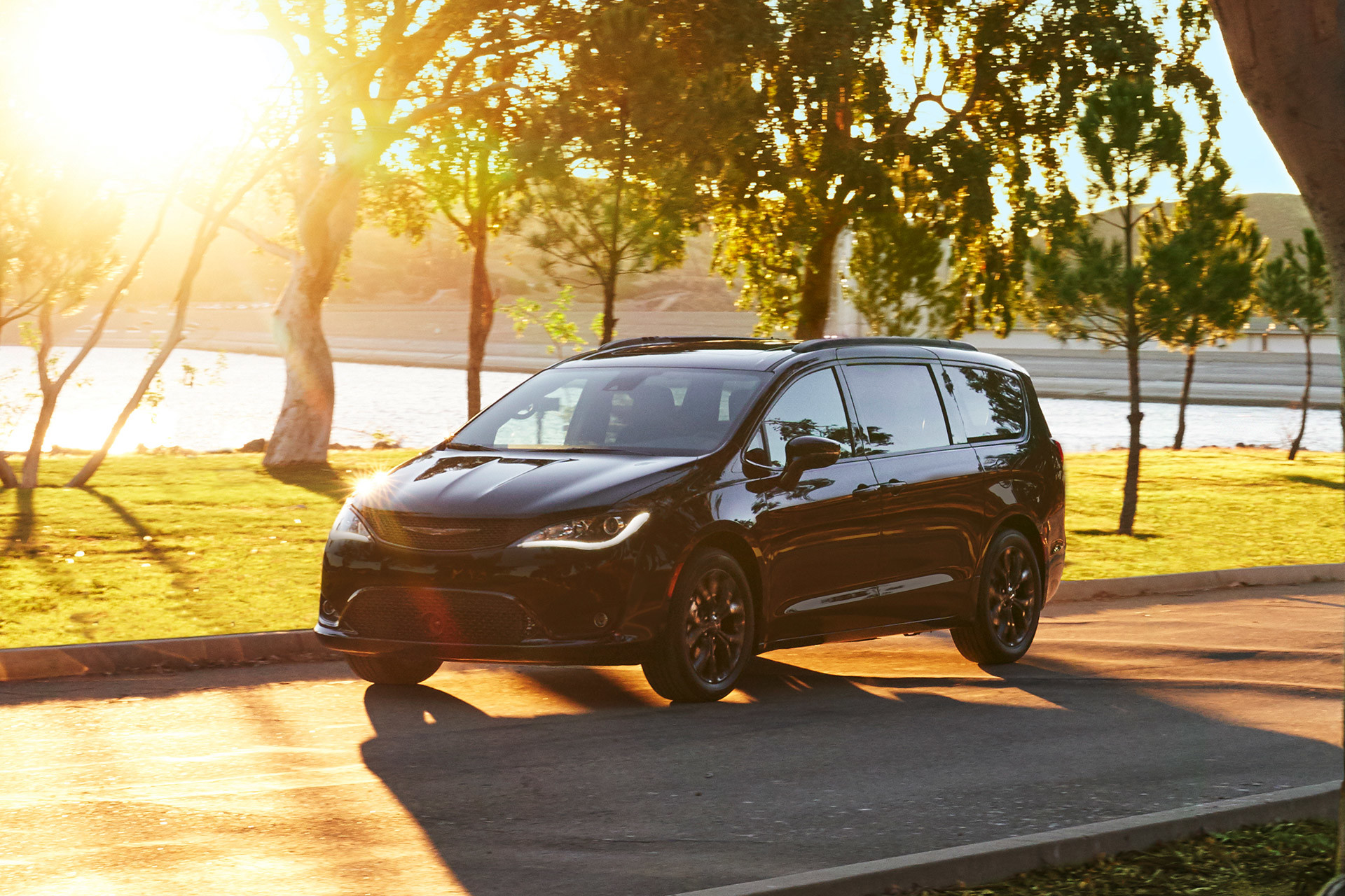 Red 2020 Chrysler Pacifica driving on a road through trees.