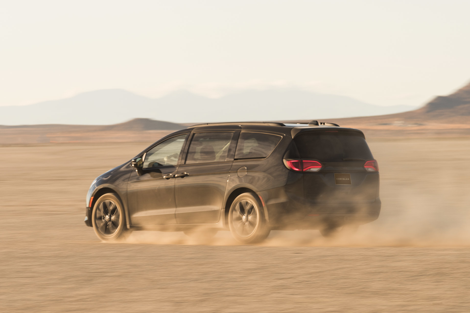Black 2020 Chrysler Pacifica driving through an open dirt field.
