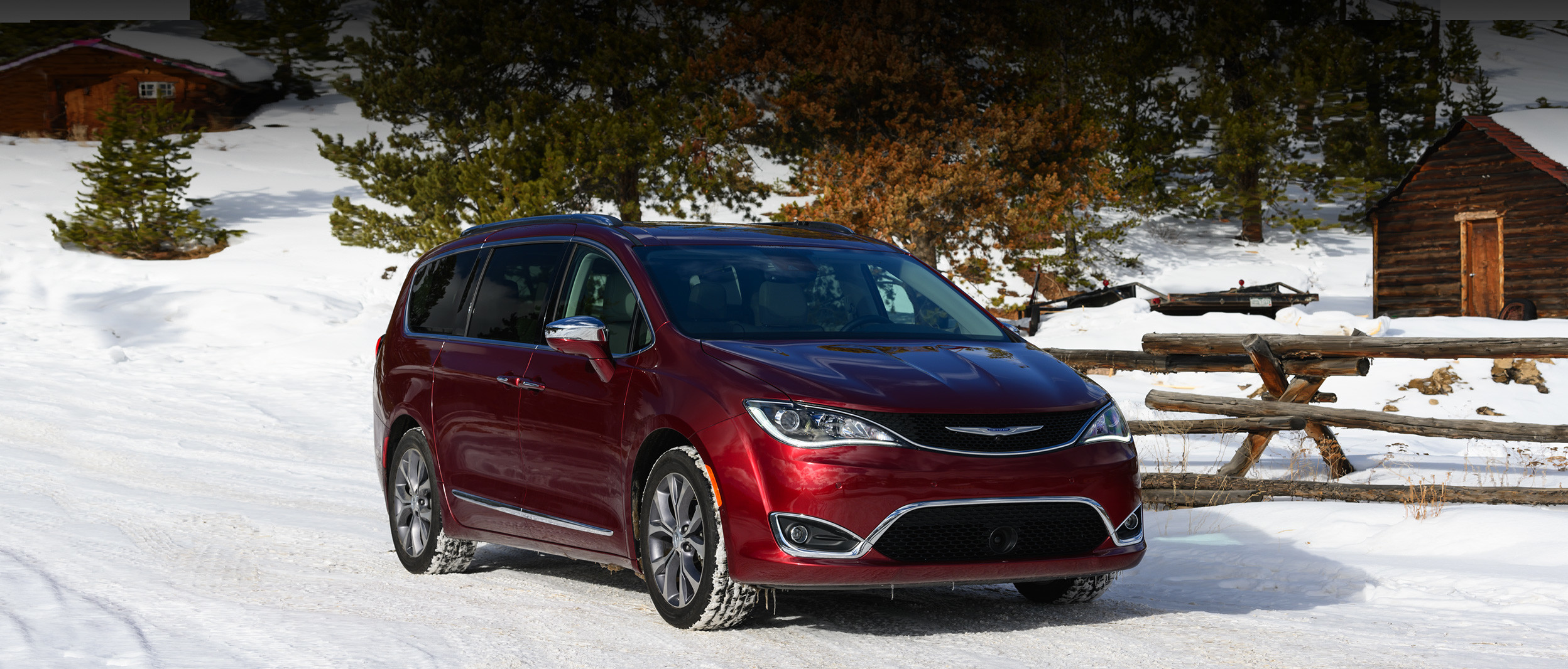 Front view of the red 2020 Chrysler Pacifica parked in a snowy forest next to a ski chalet
