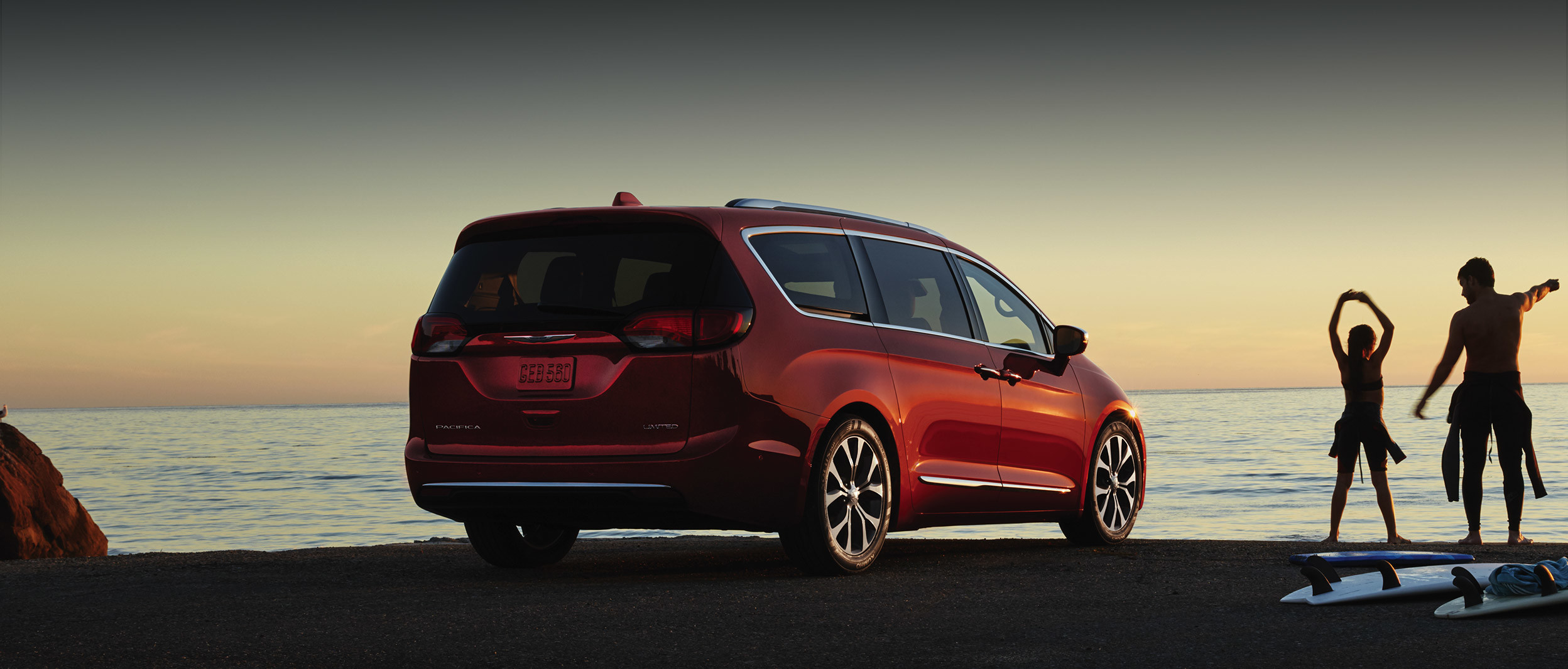 Dad and daughter with surfboards stretching next to a red 2020 Chrysler Pacifica.