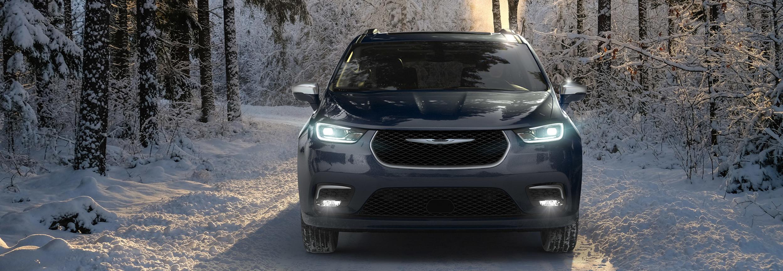 Front view of a 2021 Blue Chrysler Pacifica driving on a snow covered road.