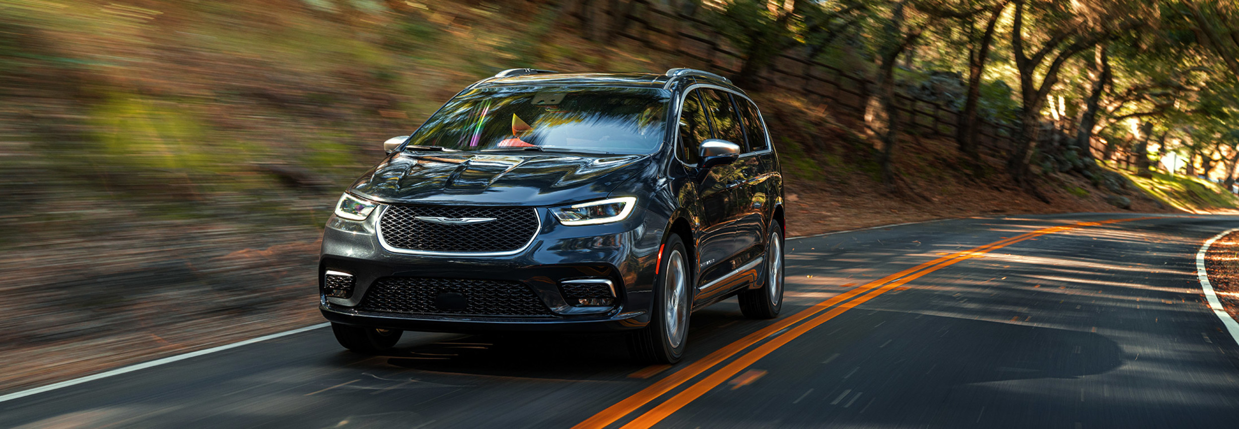 A front view of a Brilliant Black Crystal Pearl 2021 Chrysler Pacifica being driven on paved road in the countryside.