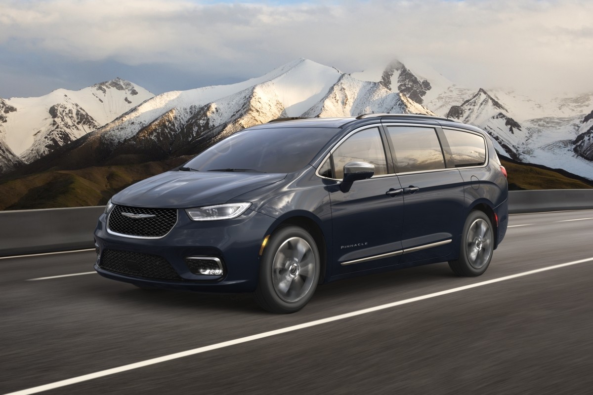 A side view of a blue 2021 Chrysler Pacifica being driven on a road in the mountains.