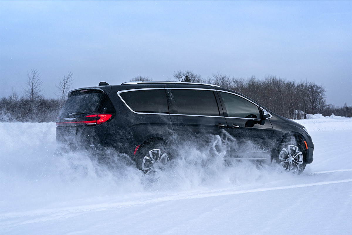 Safety First. Always. A side view of a Brilliant Black Crystal Pearl 2021 Chrysler Pacifica being driven on a snow-covered road.