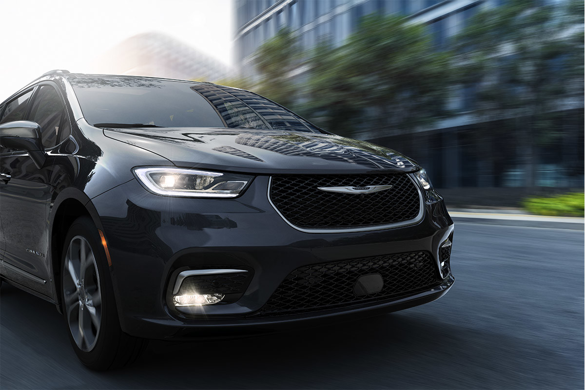 The New Look of Family Fun A front view of a Brilliant Black Crystal Pearl 2021 Chrysler Pacifica being driven past a condominium.