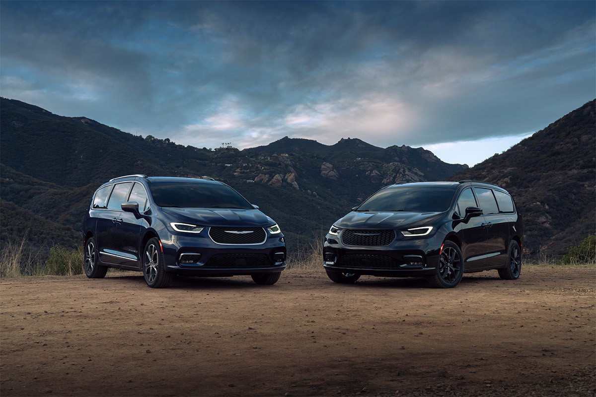 A front view of two 2021 Chrysler Pacifica minivans parked on a dirt road in front of a mountain range.