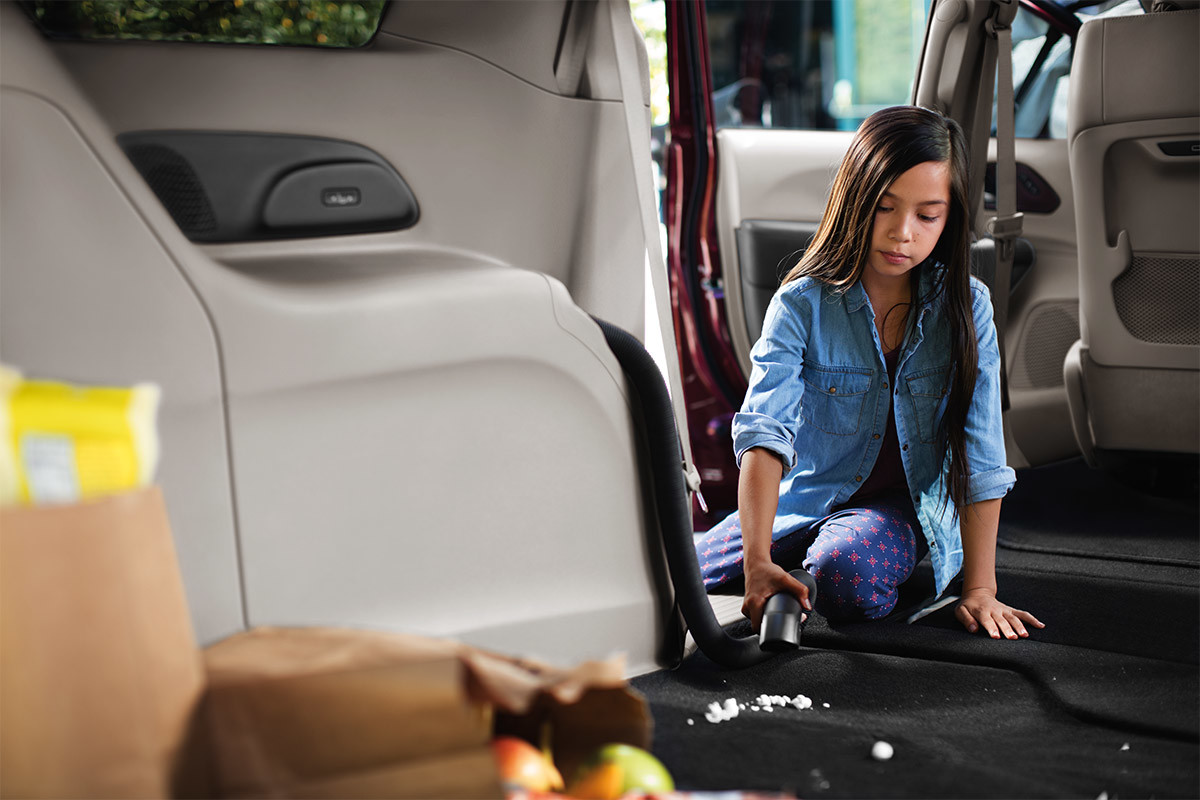 A close-up of a young girl vacuuming crumbs off the floor of a 2021 Chrysler Pacifica using the available bagless Stow ‘n Vac.