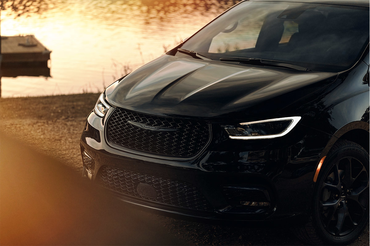 A front view of a parked Brilliant Black Crystal Pearl 2021 Chrysler Pacific as the sun sets on a lake and dock in the background.