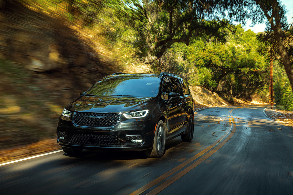 A front view of a Brilliant Black Crystal Pearl 2021 Chrysler Pacifica being driven on a tree-lined road.