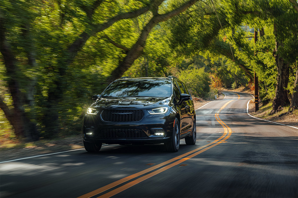 A front view of a Brilliant Black Crystal Pearl 2021 Chrysler Pacifica being driven on a tree-lined road.