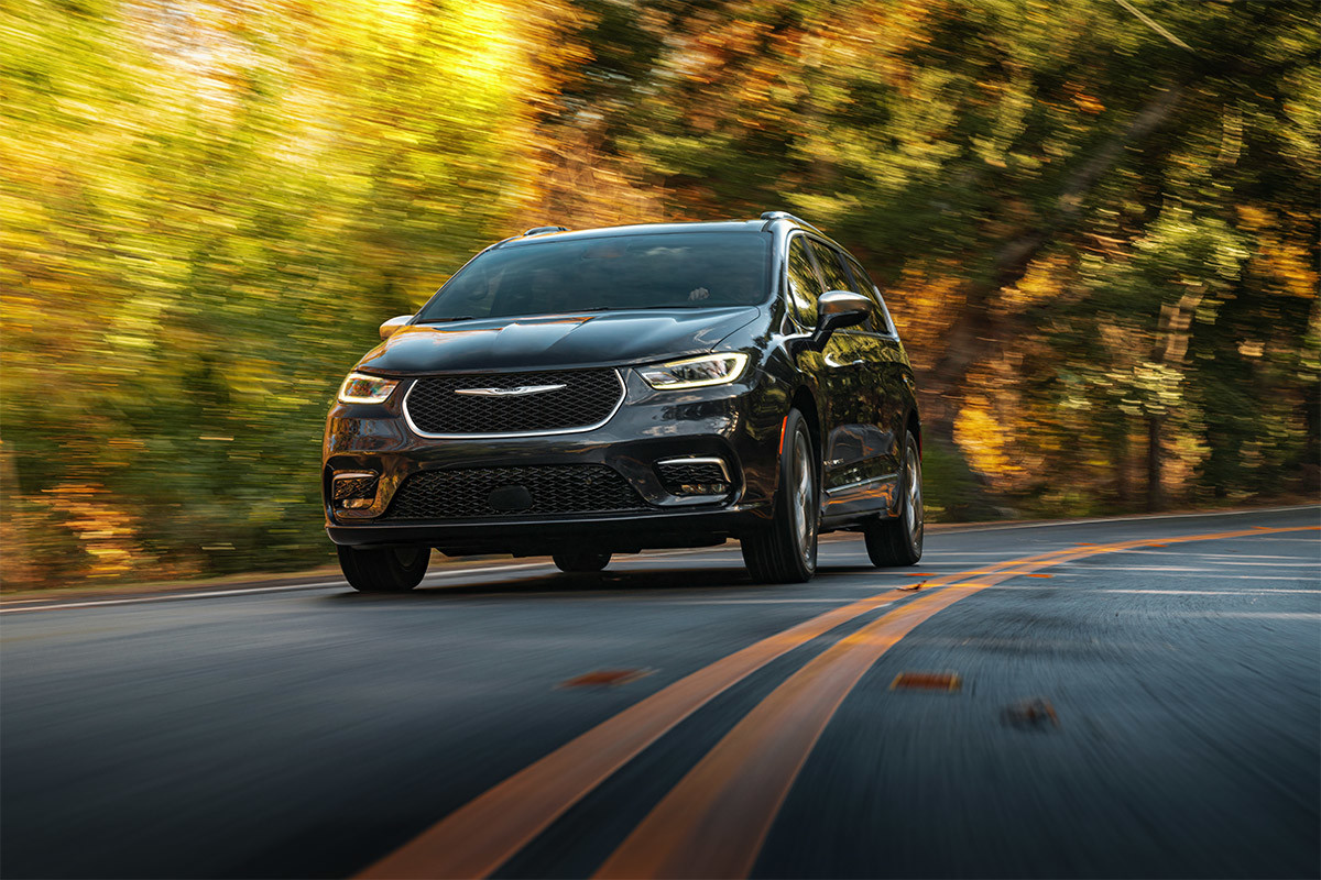 A front view of a person confidently handling a curve on a tree-lined road in a Brilliant Black Crystal Pearl 2021 Chrysler Pacifica.