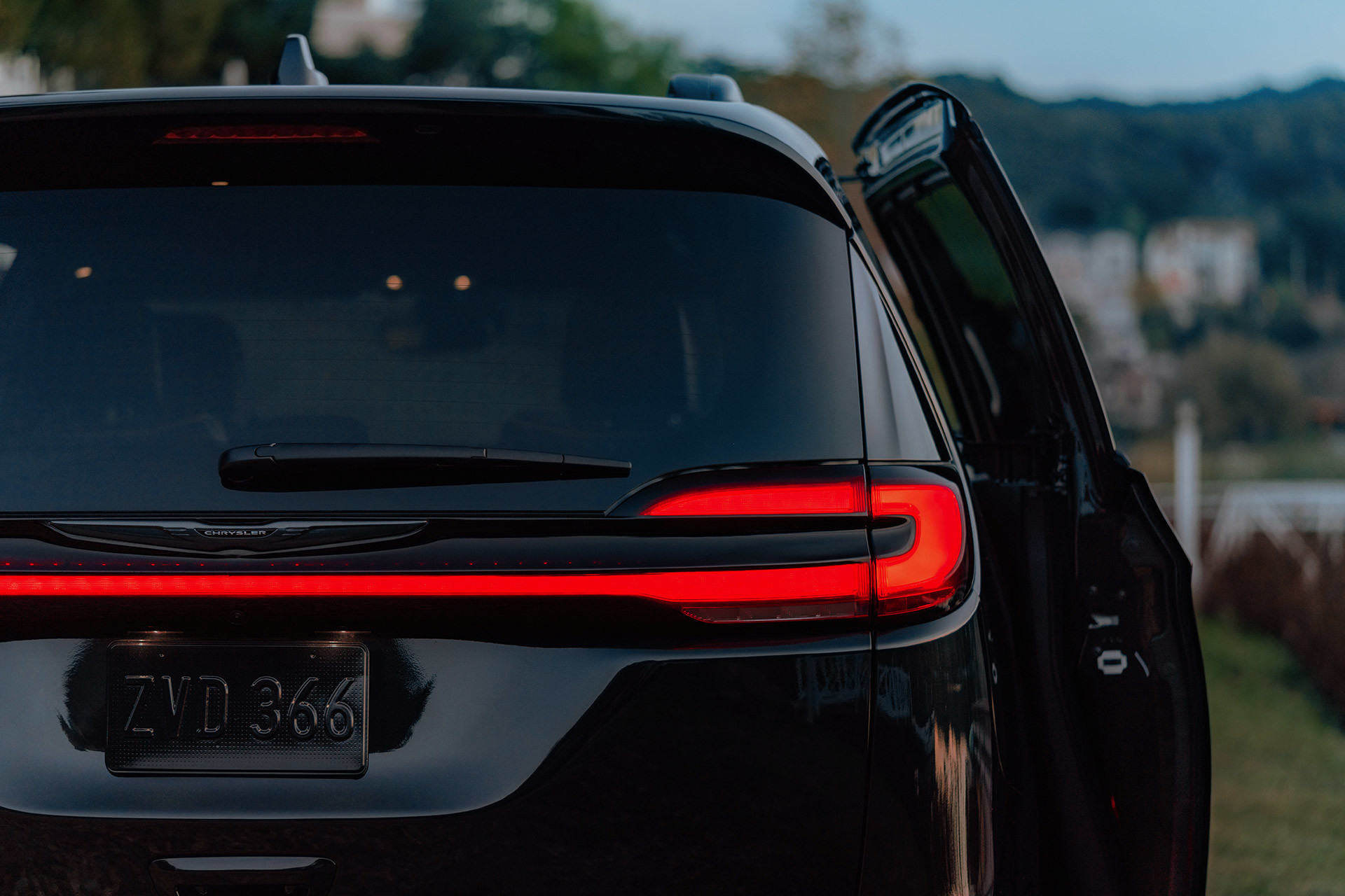 Vue arrière en gros plan des feux arrière à DEL pleine largeur d’une Chrysler Pacifica 2021 à couche nacrée cristal noir étincelant garée au bord d’un lac.