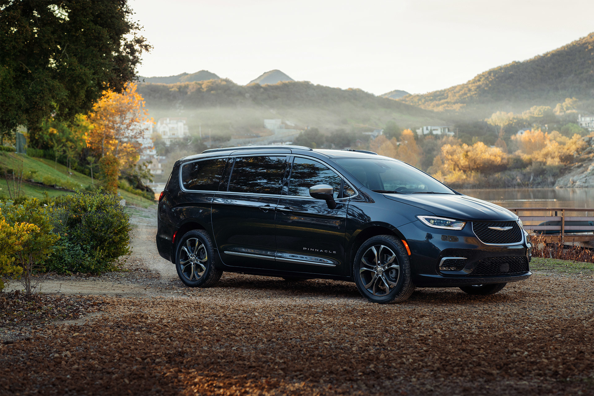 Vue latérale d’une Chrysler Pacifica 2021 garée sur une route de gravier avec des collines brumeuses en arrière-plan.