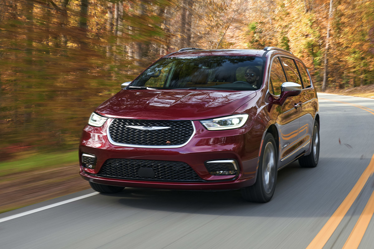 Angled view of a Red Chrysler Pacifica driving with trees in background.