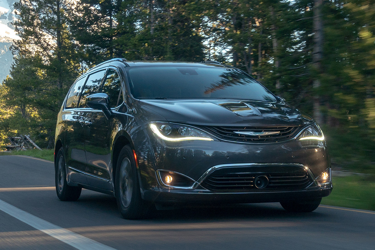 Une Chrysler Pacifica Hybrid 2019 grise roulant sur une route pavée dans la forêt.