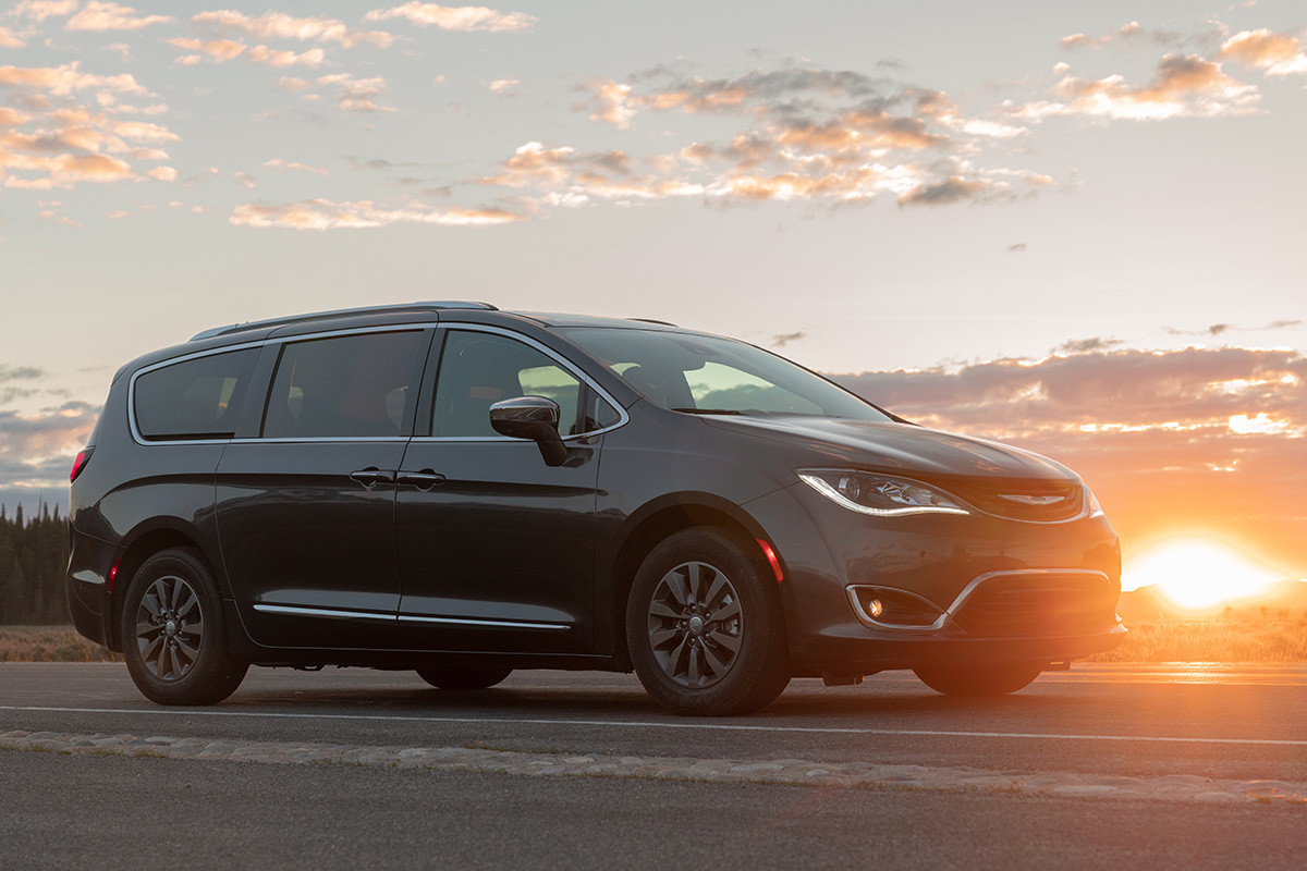 Une Chrysler Pacifica Hybrid 2019 grise garée dans un stationnement extérieur avec une prairie et des arbres en arrière-plan.