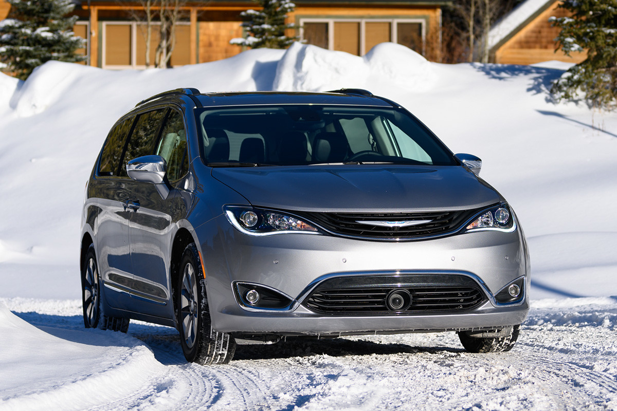 Vue de face de la Chrysler Pacifica 2020, illustrée en argent, roulant sur une route enneigée, avec un grand chalet en arrière-plan