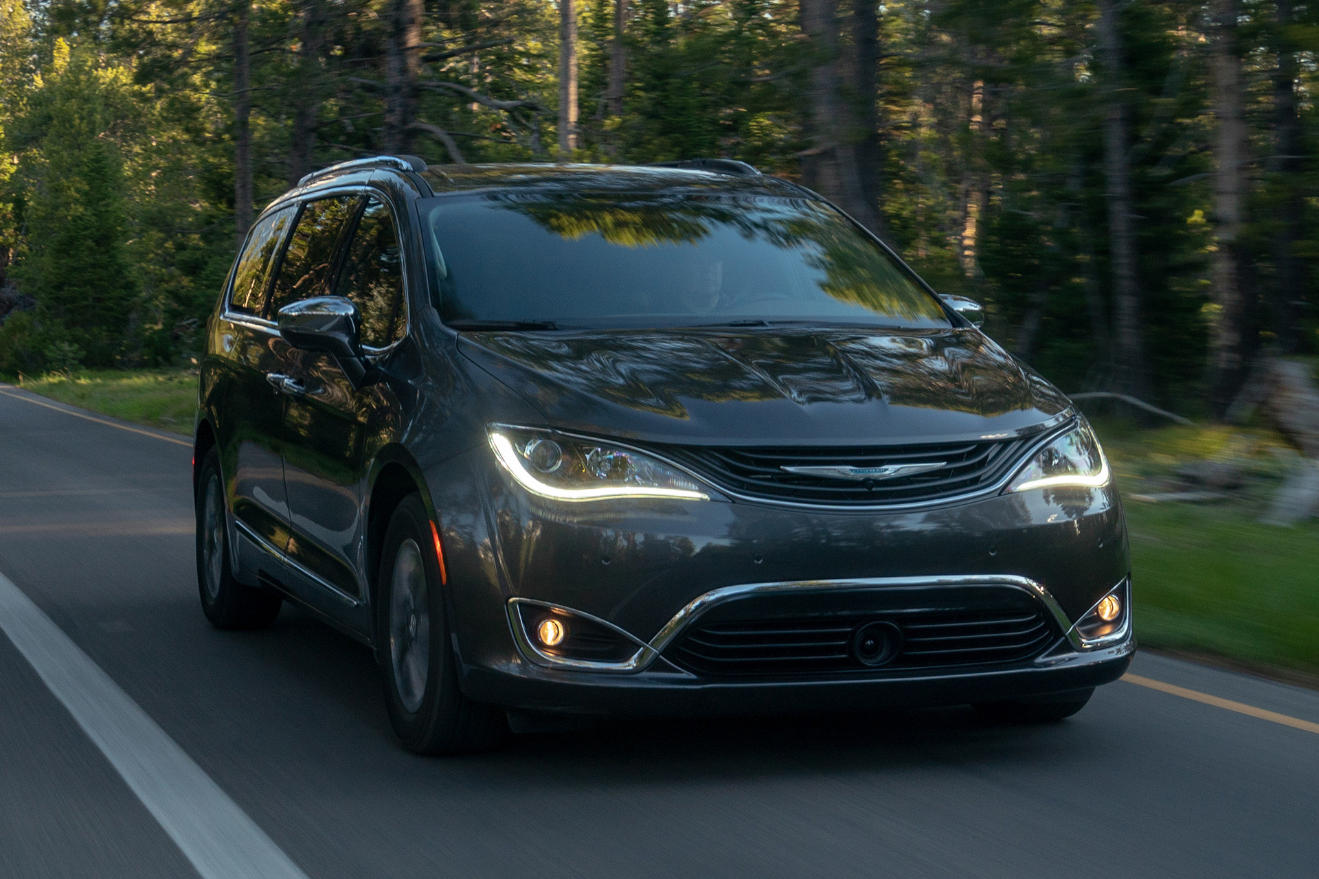 Grey 2019 Chrysler Pacific Hybrid being driven on a paved road through a forest.