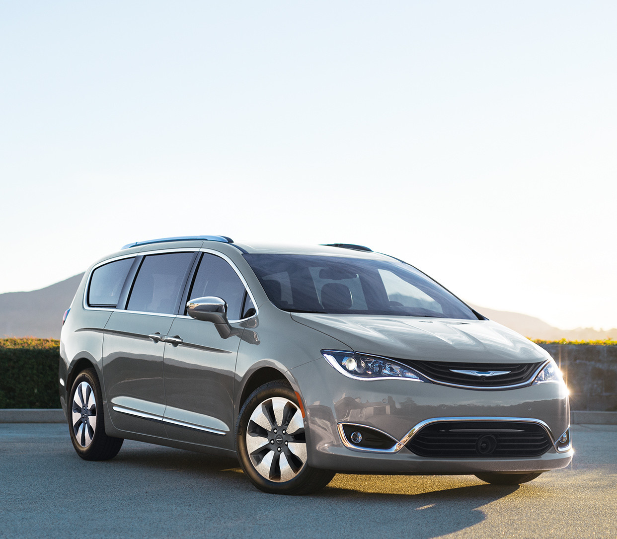Une Chrysler Pacifica Hybrid 2019 couche blanc perlé garée dans un stationnement extérieur avec un champ et des montagnes en arrière-plan.