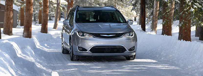 Vue de face de la Chrysler Pacifica Hybrid 2019, illustrée en argent, roulant sur une route enneigée dans la forêt