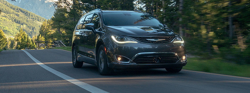 Une Chrysler Pacifica Hybrid 2019 grise roulant sur une route pavée dans la forêt, en montagne.