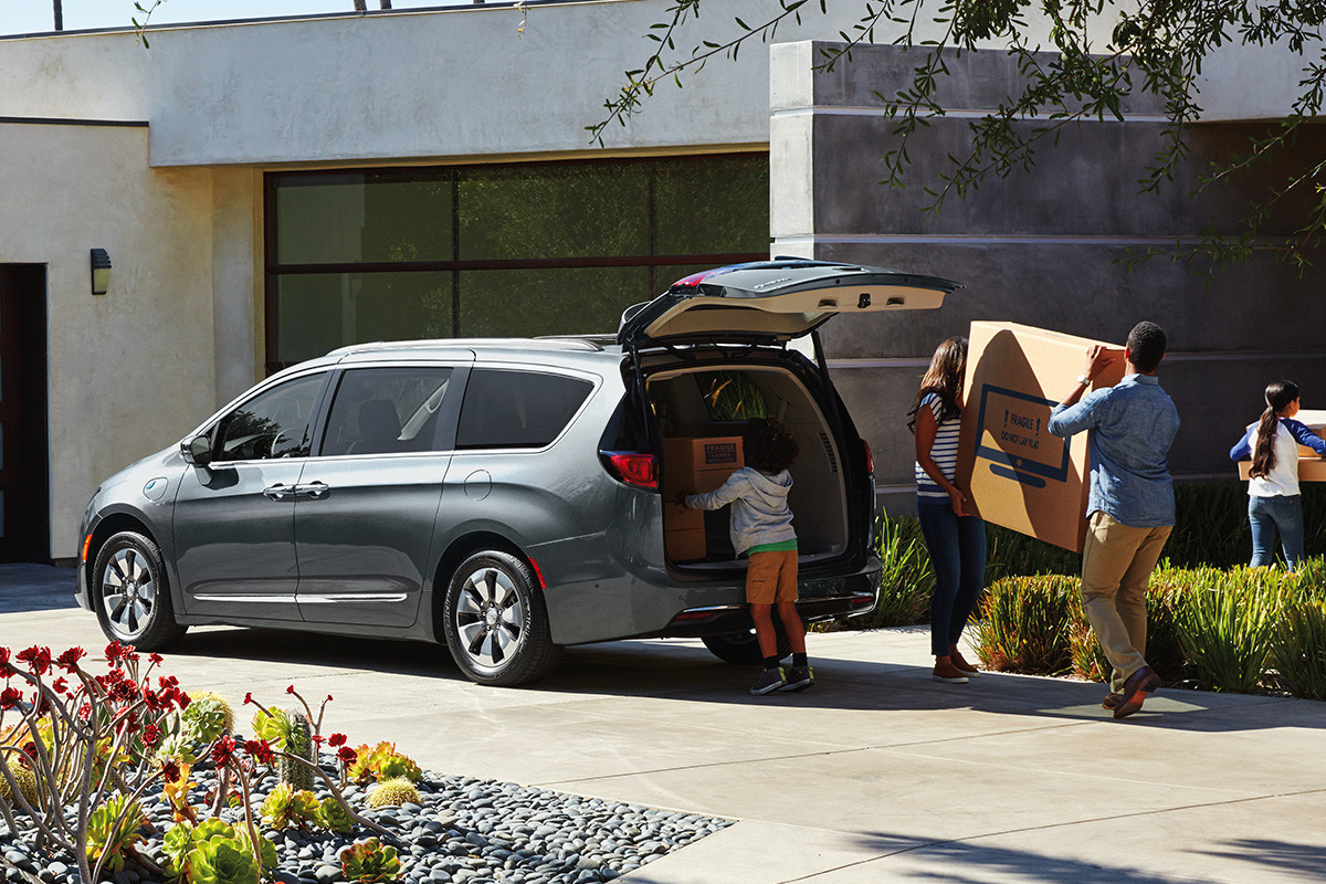 The 2020 Chrysler Pacifica Hybrid parked on a driveway with its trunk opened while people unload cargo