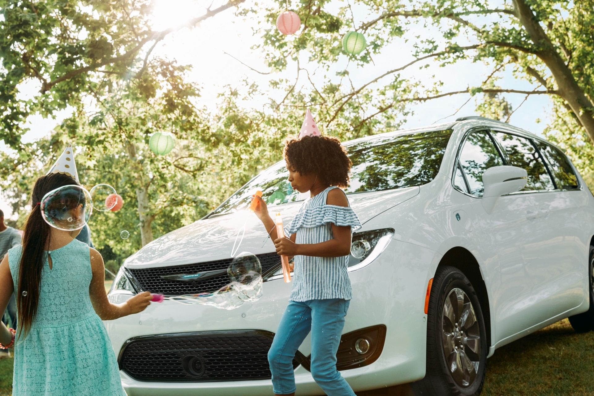 Chrysler Pacifica Hybrid 2020 blanche stationnée dans un parc, à côté de deux enfants qui jouent.