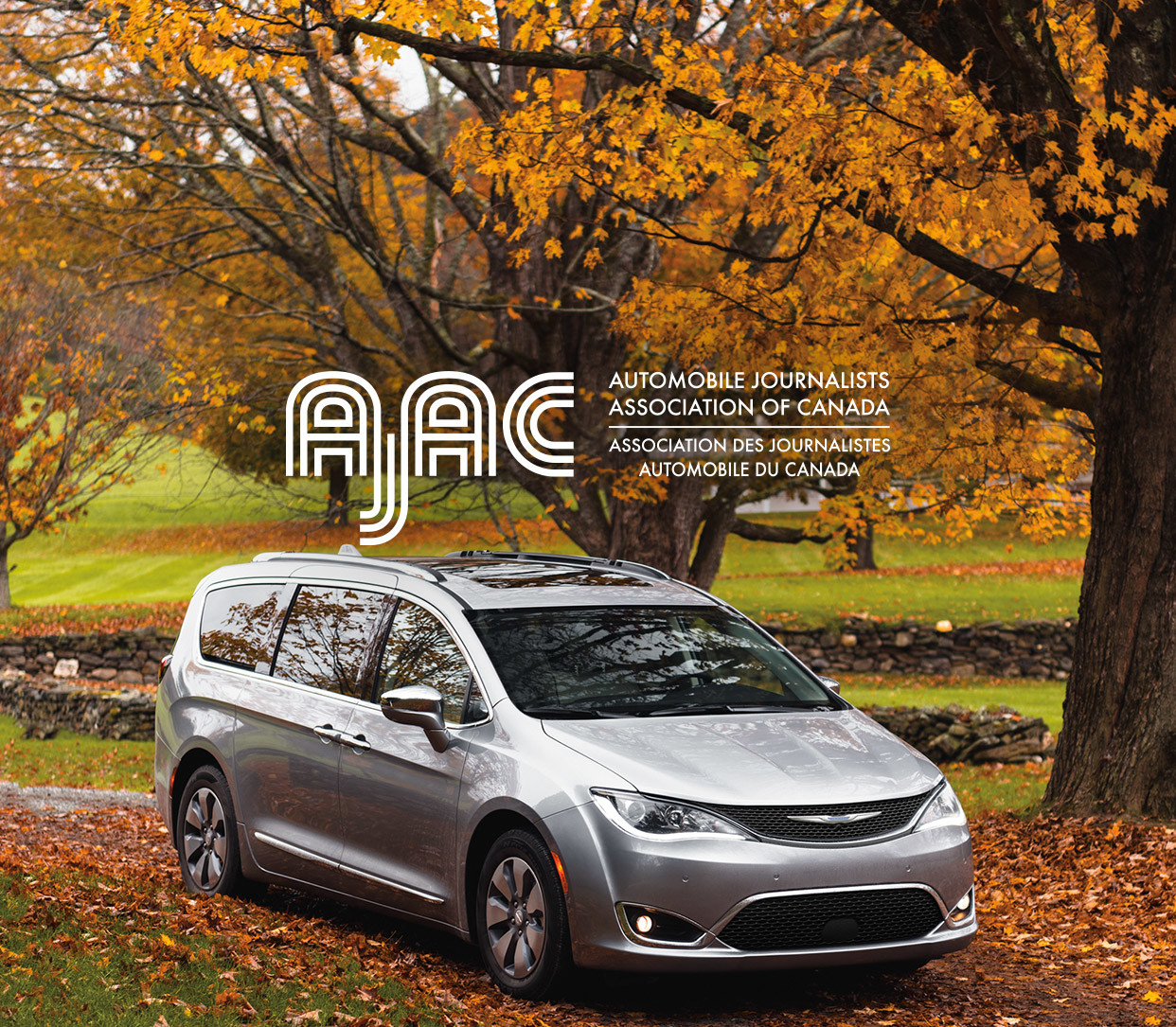 A silver 2020 Chrysler Pacifica Hybrid parked on a road with fallen leaves on the ground