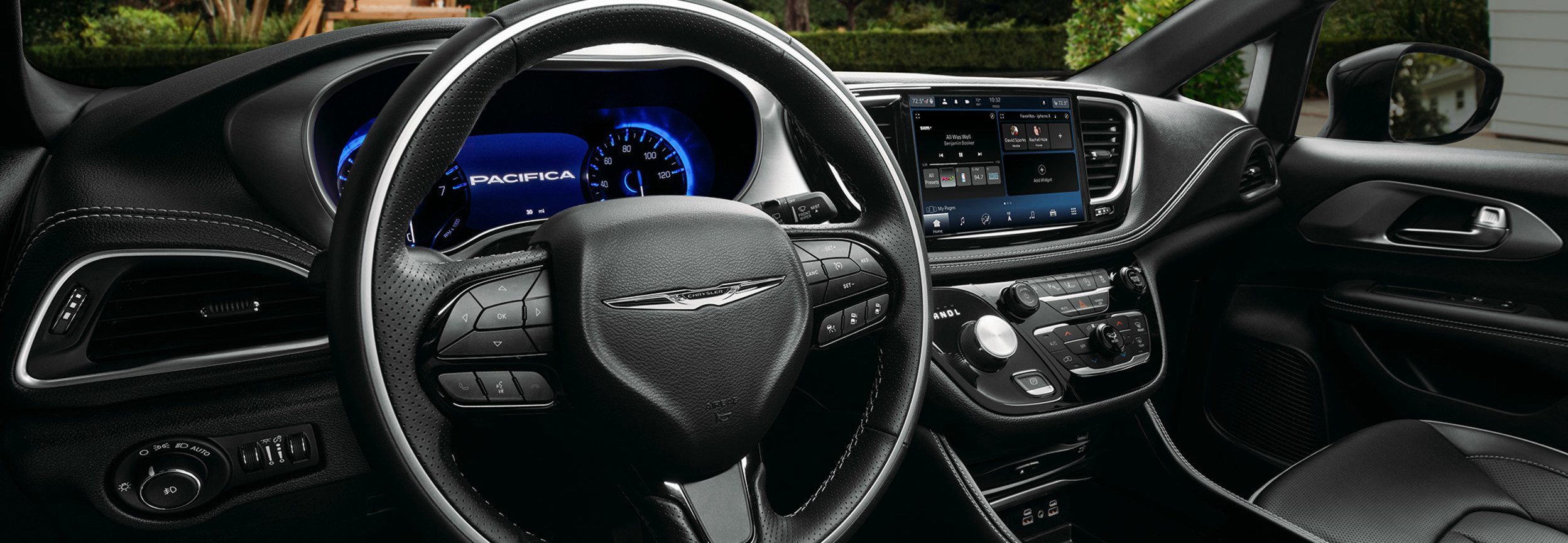 Vue du siège du conducteur d’une Chrysler Pacifica 2021 garée dans une entrée avec une cour et une remise en arrière-plan