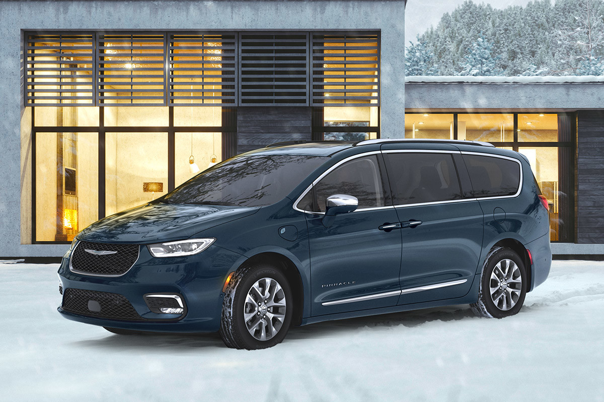 Vue latérale d’une Chrysler Pacifica Hybrid 2021 stationnée devant un bâtiment industriel bien éclairé en hiver