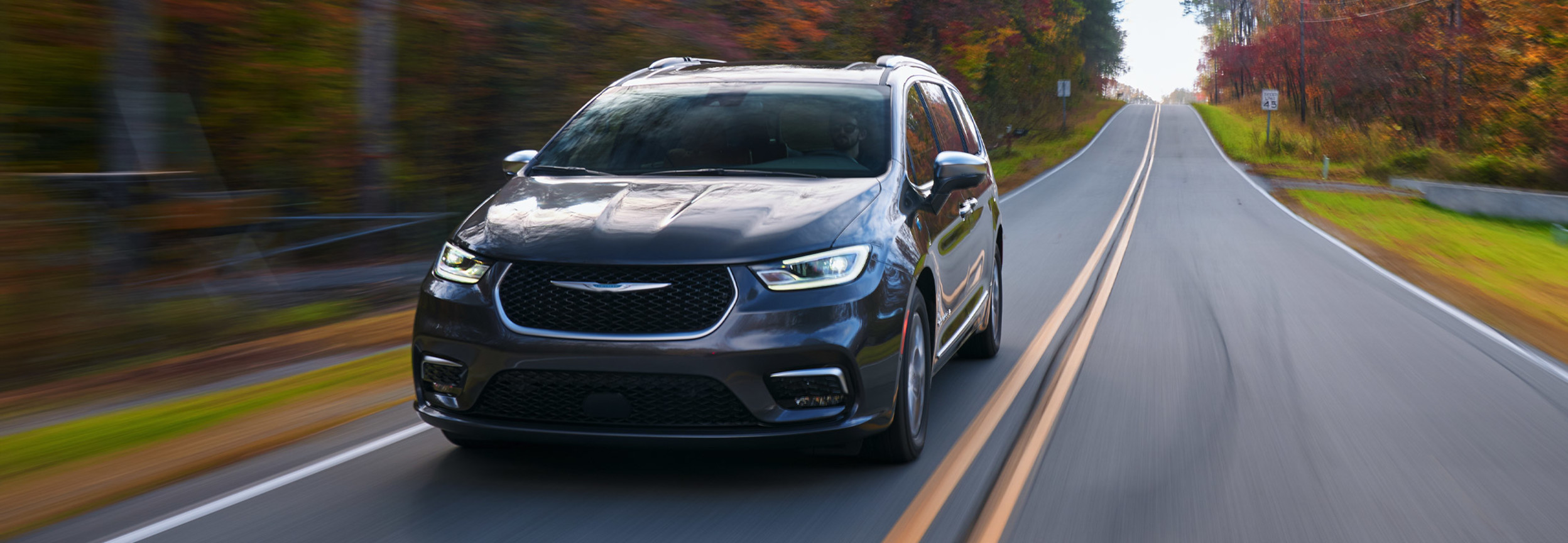 Une Chrysler Pacifica Hybrid 2022 grise roulant sur une route forestière