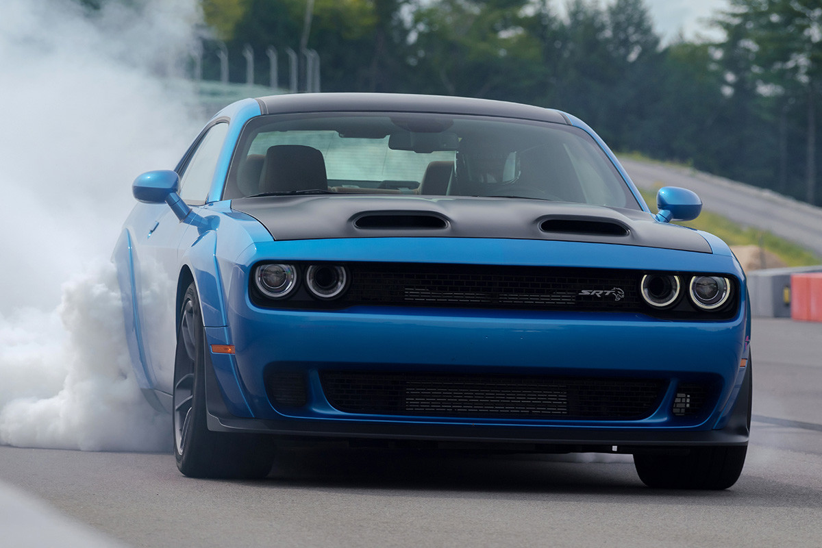 Blue 2019 Dodge Challenger burning out, with smoke coming from the rear tires, on an outdoor racing track.