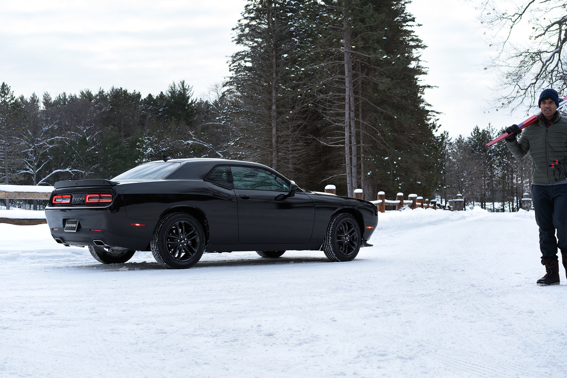 Rear view of the black 2019 Dodge Challenger parked in the snow while a man walks by with skis