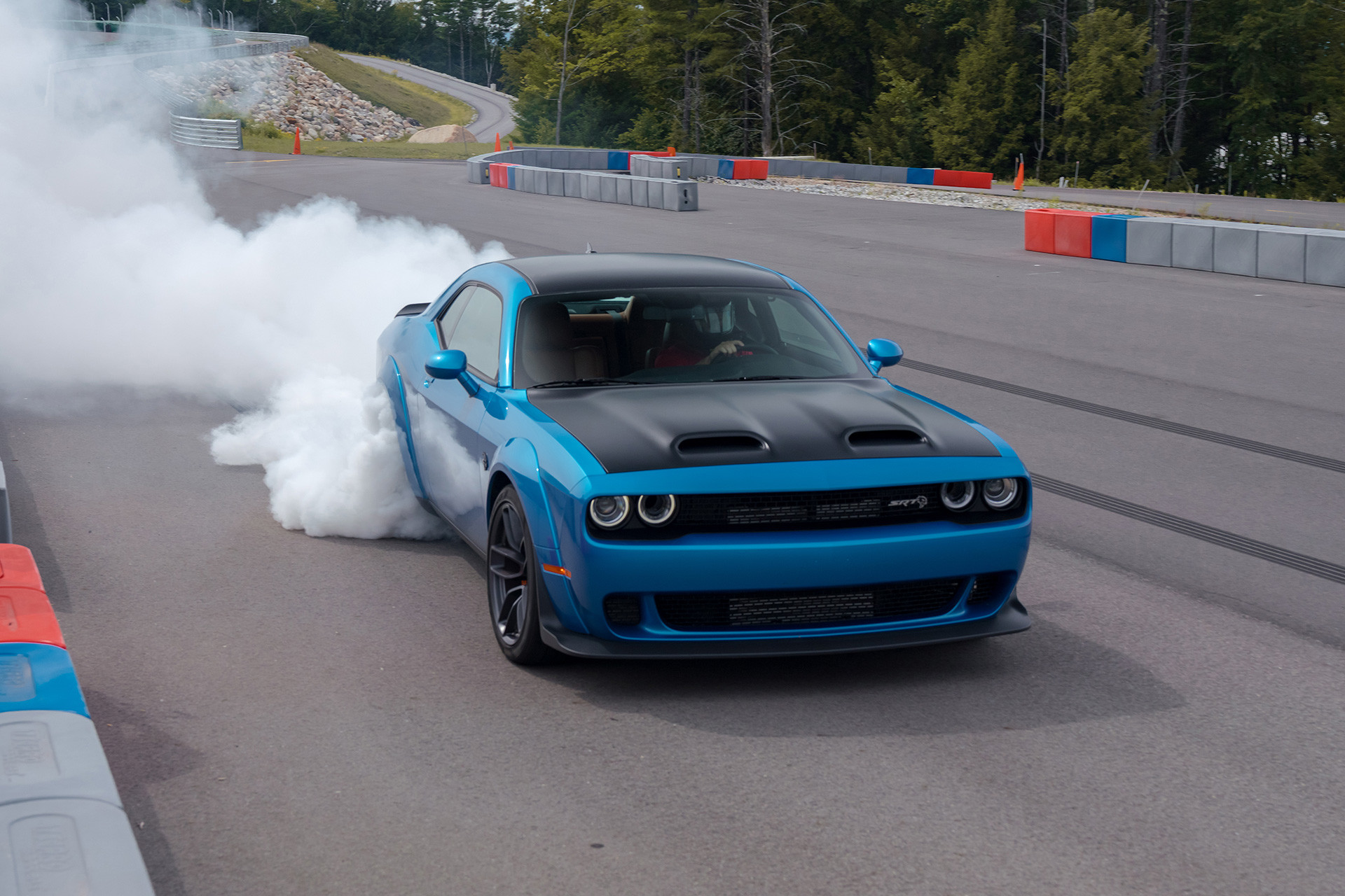 Une Dodge Challenger 2019 bleue sur un circuit extérieur; les roues patinent et de la fumée s’échappe des pneus arrière.