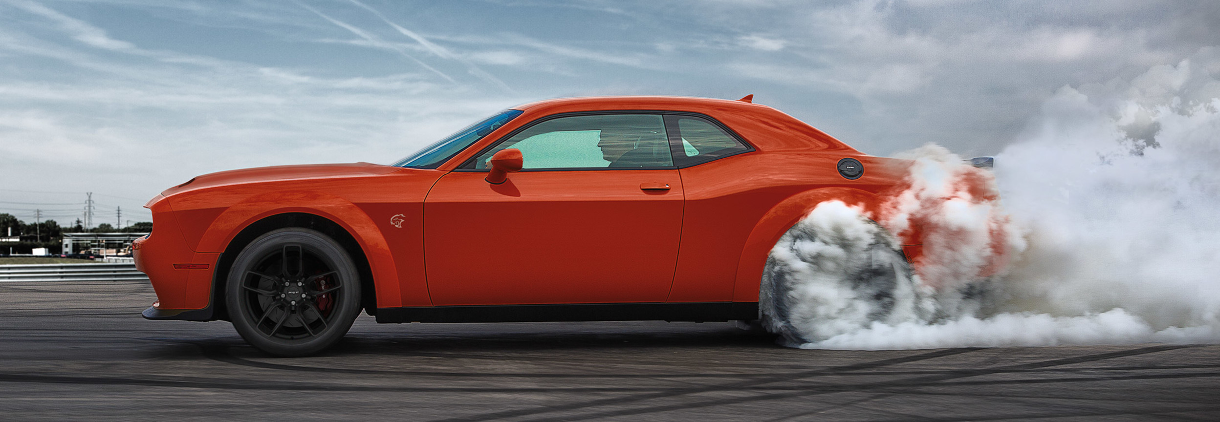 Dodge Challenger 2020 orange accélérant dans une aire de stationnement vide.