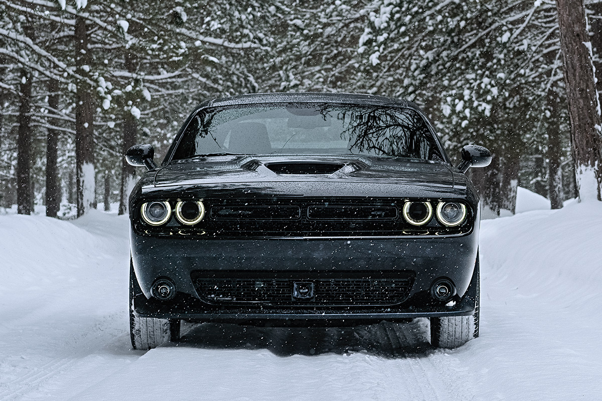 Front view of the black 2020 Dodge Challenger driving on a snow-covered road in a forest